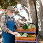 Agricultor idoso em uma banca ao ar livre, com frutas e verduras coloridas à venda