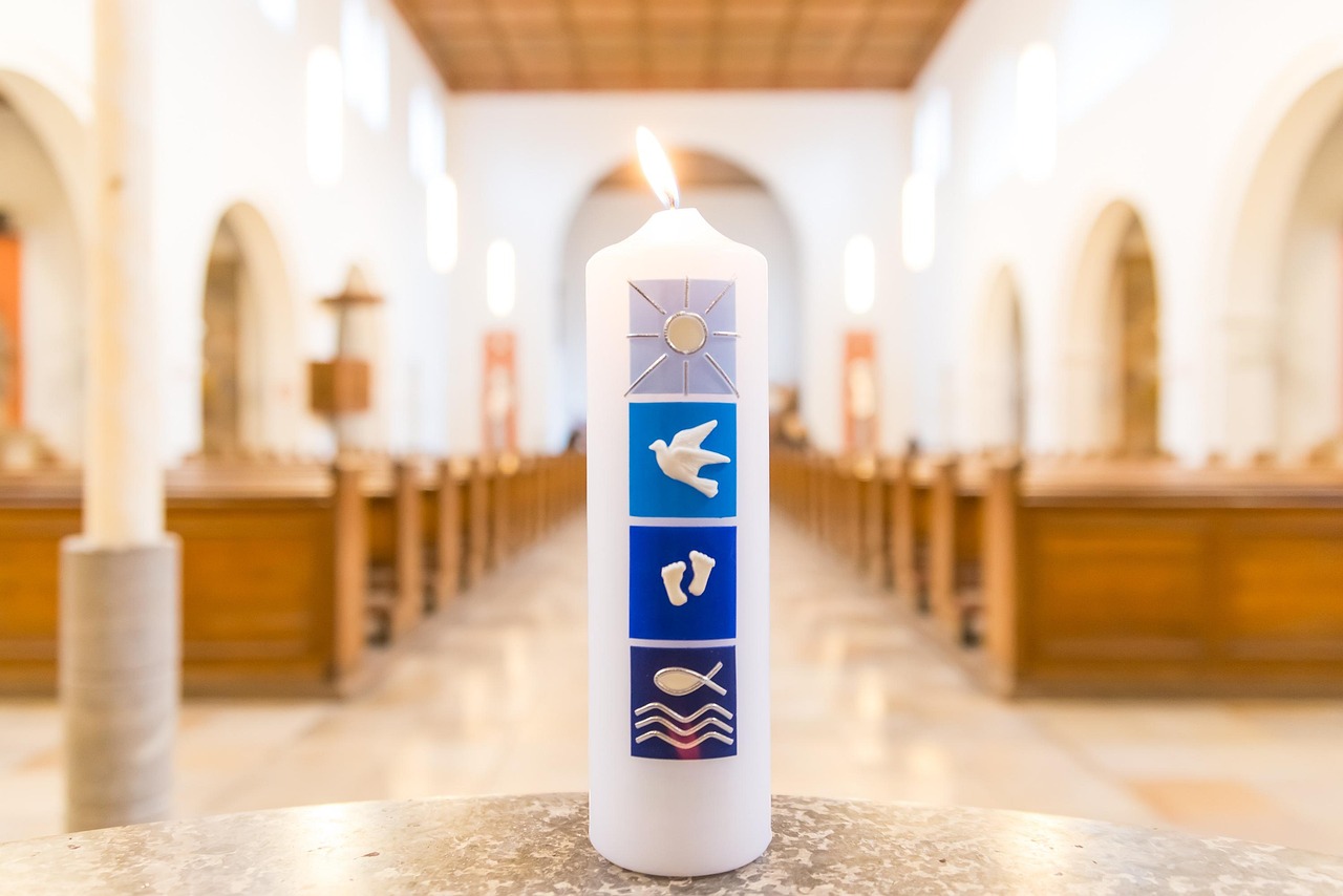 Interior de uma igreja com uma vela junto a uma pia batismal, em referência ao rito cristão do batismo.